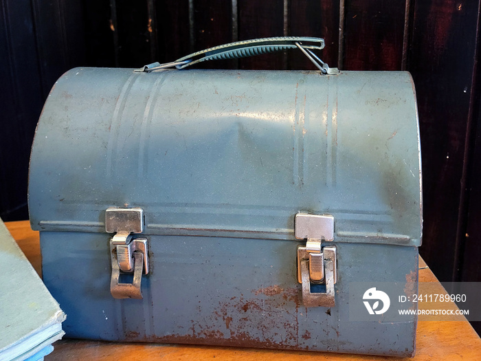 Old dented blue metal lunch pail with a book on a wooden table