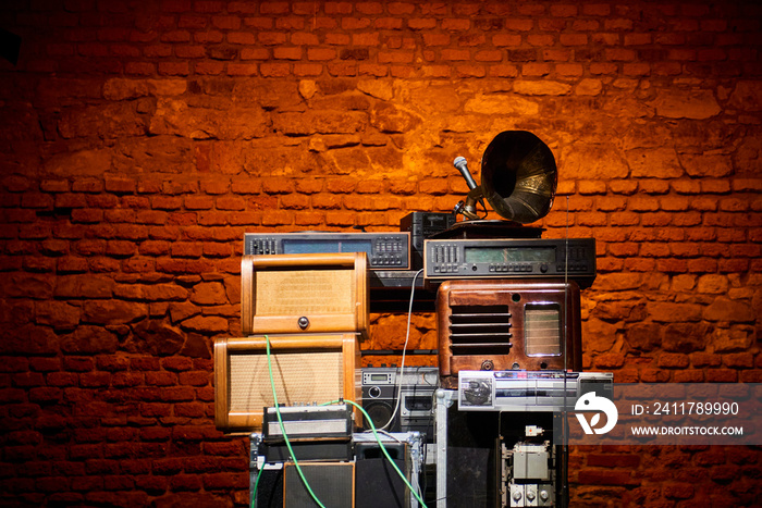 Tower built from old disused analog radios, amplifiers, cassette recorders and a phonograph. Old brick wall background. Selective focus