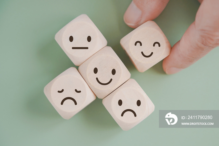 hand selected happy face wood cube and others on green background for customer service evaluation, feedback, satisfaction survey or mental heath concept