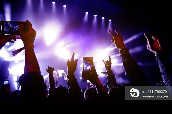 Crowd of people having fun while watching concert show at music festival. Raised hands with mobile phones.