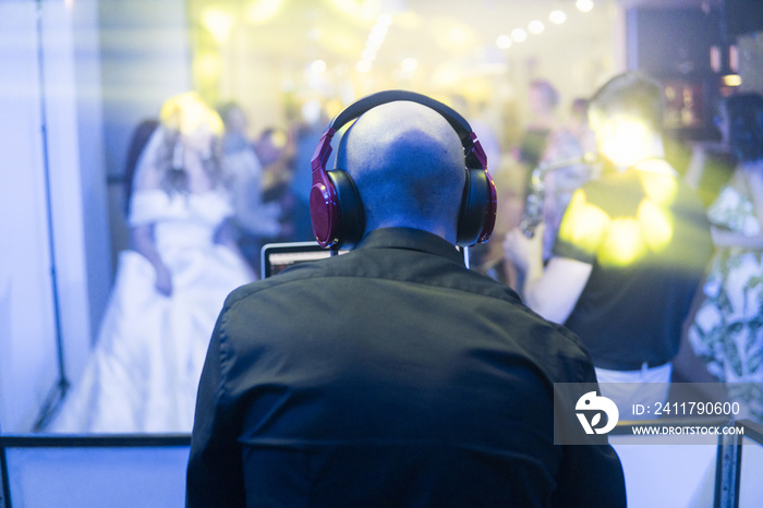 DJ with red headphones at night club party under the blue light and people crowd in background. Charismatic disc jockey at the turntable.