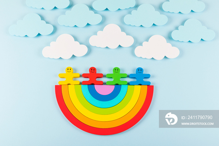 International Children’s Day background. Wooden toy children with the rainbow on the light blue background. Flat lay. Copy space.