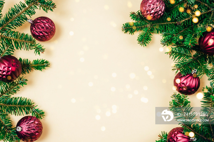 Fir branches and purple Christmas baubles with golden bokeh lights on beige background. Top view, flat lay, copy space