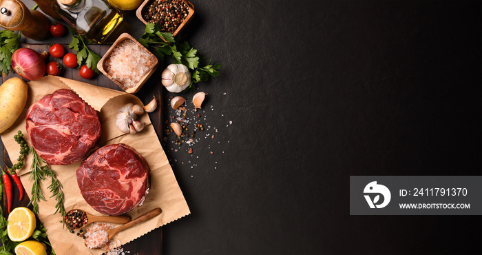 Fresh raw pieces of beef meat with ingredients for cooking on panorama black stone background