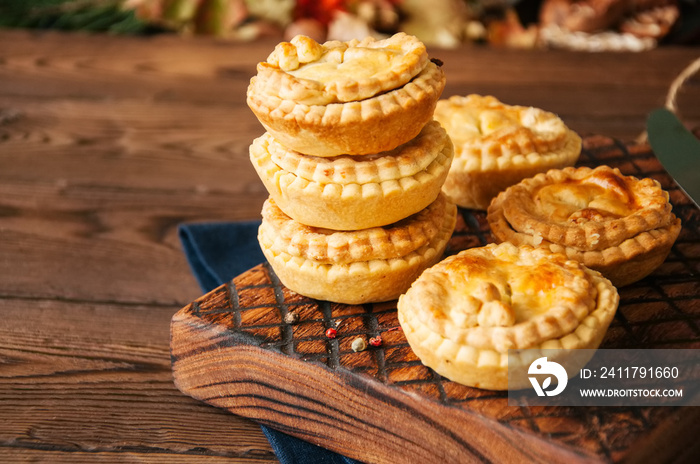 Mini meat pies from flaky dough on a wooden board over wooden background.