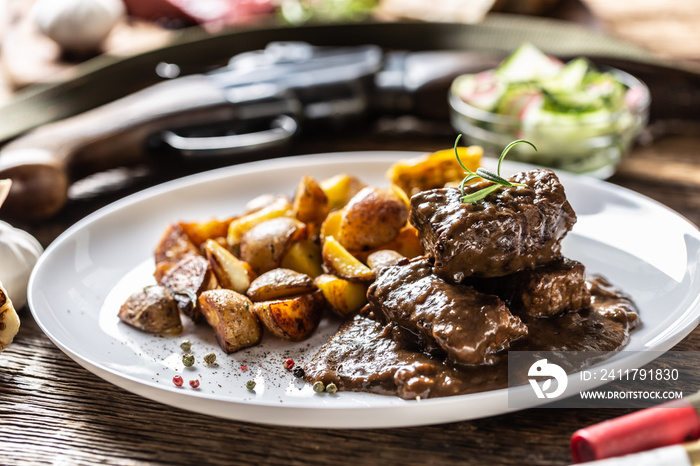 Wild game goulash stew served with roasted potatoes and seasoned with four colour pepper corn. Whole food is surrounded by hunting shotgun and gun bullets.