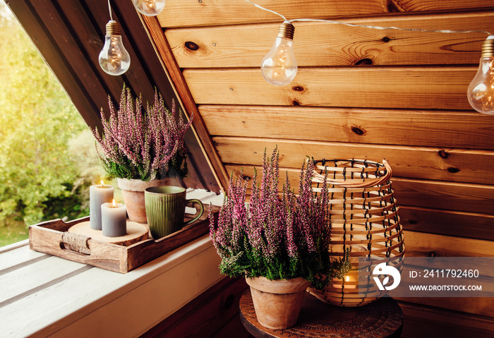 Small natural color wooden cabin balcony with heather flowers, candlelight flame and steaming cup of tea coffee. Cute autumn hygge home decor arrangement.