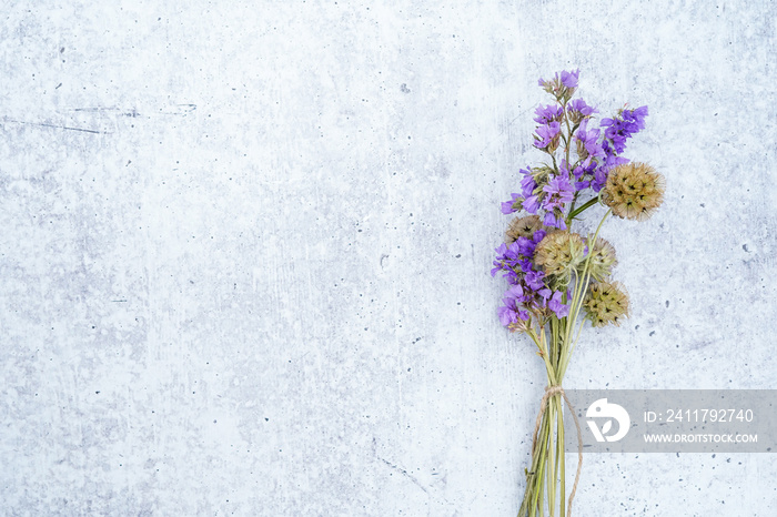 Bouquet of starflower seed pods and purple statice flowers tied with a twine bow. Concrete background. Space for text.