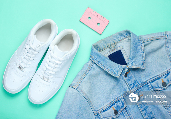 Retro style denim stylish jacket, audio cassette and white hipster sneakers on a mint-colored paper background. Minimalism, pop culture, top view.