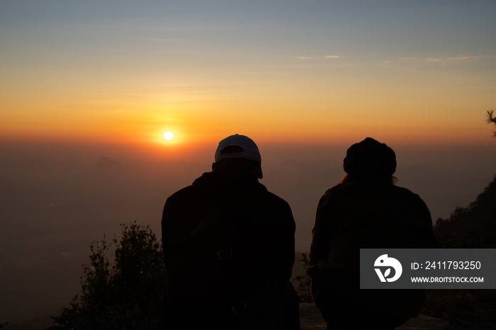 Image of sunrise on orange and yellow horizon with a silhouette of a couple in natural surrounding ( Phu kradueng Thailand )