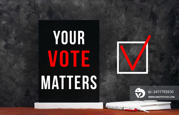 Your Vote Matters text sign on black chalkboard with white notebok and red pen on dark background. Message written on blackboard display. Vote elections concept. Make the political choice.