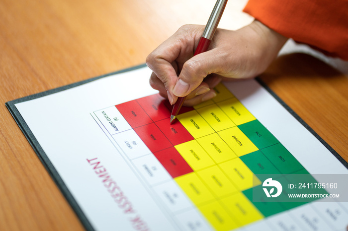 Action of a person is using ballpoint pen to marking on the risk assessment matrix table at  High risk  level. Industrial or business working action scene photo. Close-up and selective focus.