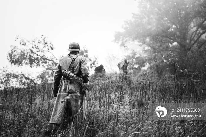 Single Re-enactor Dressed As German Wehrmacht Infantry Soldier In World War II Walking In Patrol Through Autumn Forest. WWII WW2 Times. Photo In Black And White Colors.