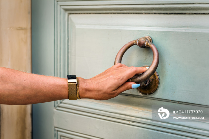 Close-up woman hand knocking wooden olive colour wooden door, in front of the house