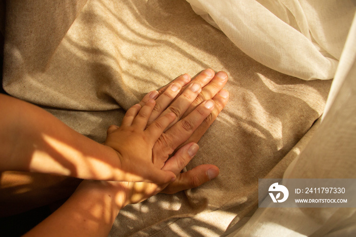 Hands of parents and child on a background of brown fabric with sunlight. Family and support concept. Top view