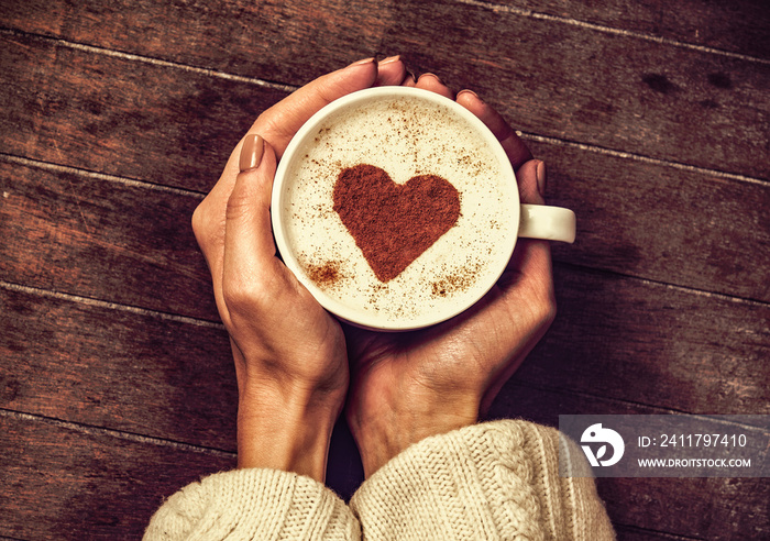 woman holding hot cup of coffee with heart shape symbol. Above view