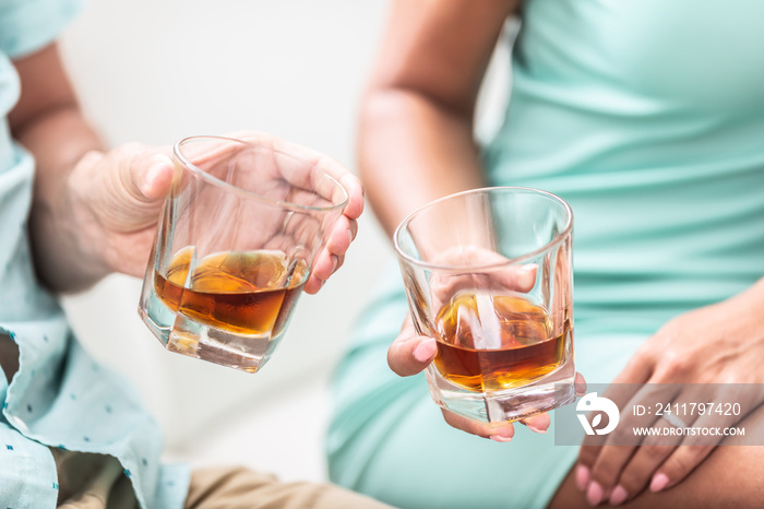 Man and woman hands toasting with glasses of whiskey brandy or rum indoors - closeup