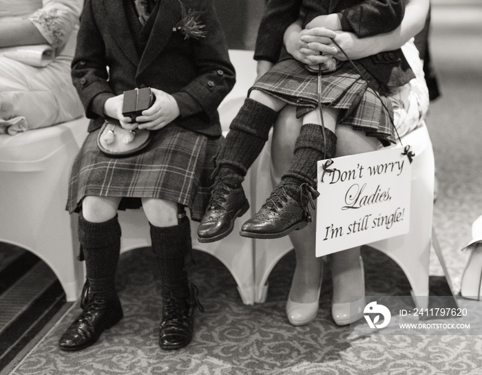 Two little page boys in kilts sit at a wedding ceremony