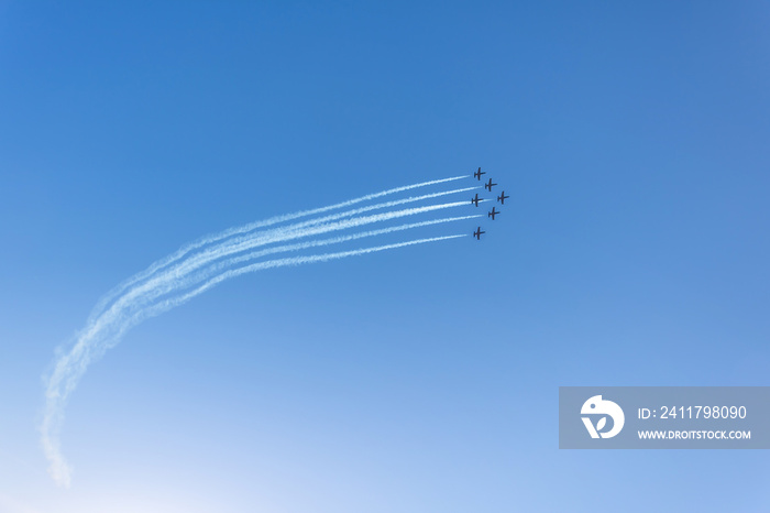 Silhouette of an airplane performing acrobatic flight on blue sky. Trace of smoke behind.