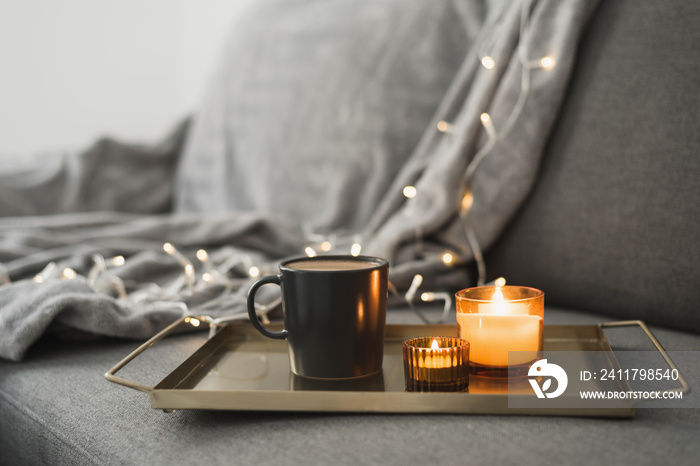 Hot coffee and two burning aroma candles on a metal tray, cozy atmosphere at home