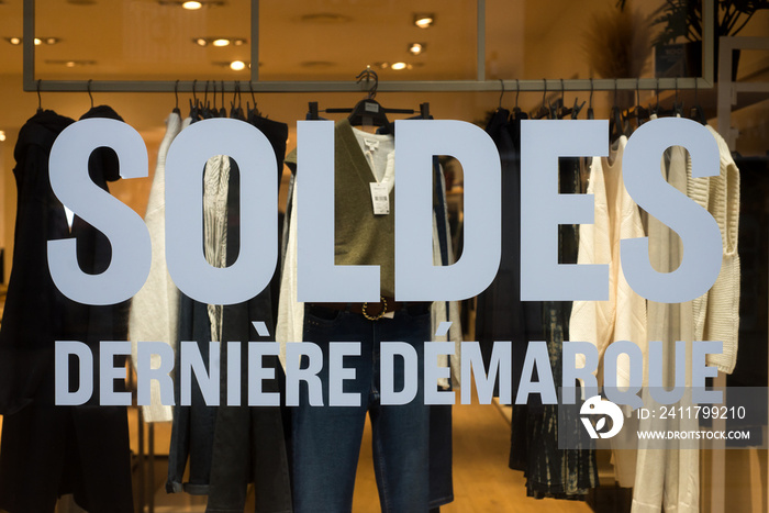 Closeup of discount sign  SOLDES derniere demarquej  in french,  the traduction of  (sales last set in english) on the window of fashion store