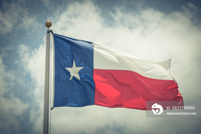 Large Texas (The Lone Star) flag waving on flag pole with cloud blue sky. Windy and sunny day with waving flag blowing/flowing. Ruffled Texas flag. Room for text, copy space. Vintage tone.