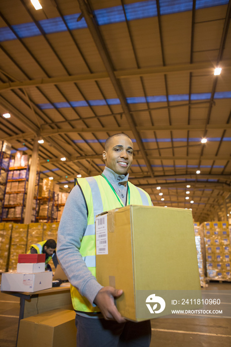 Portrait confident male worker carrying box in distribution warehouse