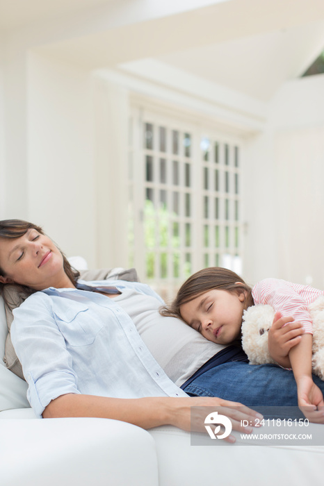 Serene pregnant mother and daughter cuddling on sofa