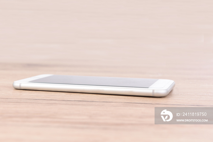 White mobile phone placed on wood desk.