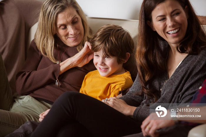 Cheerful boy sitting with mother and grandmother on sofa at home