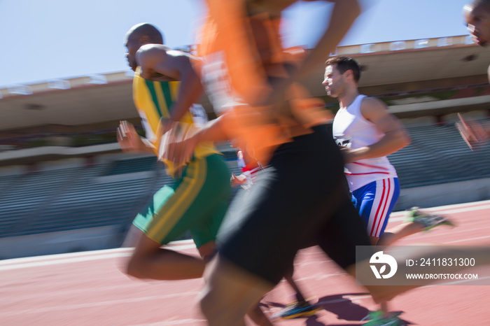 Male track and field athletes racing on sunny sports track