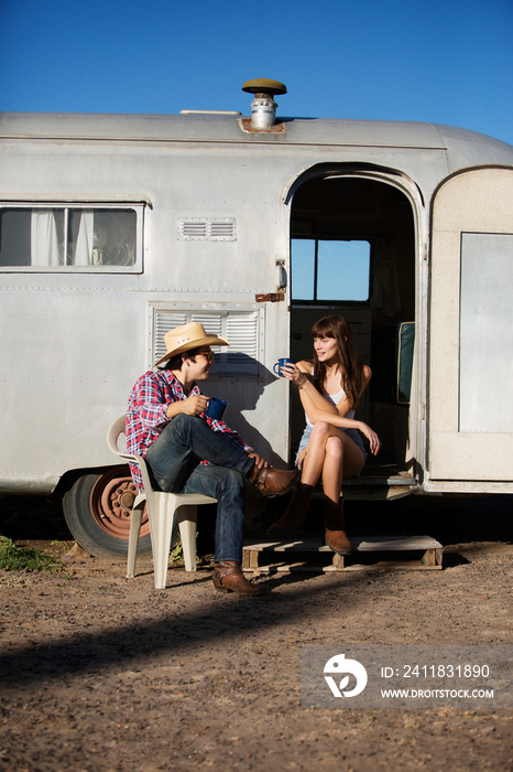 Young couple sitting by travel trailer