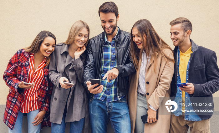 Group of people standing by the wall and using their smartphones- A boy showing his friends a photo 