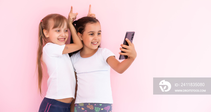 two little girls with a smartphone on a pink background