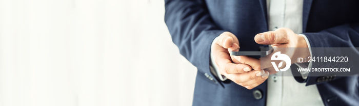 Businessman in blue suit holding a black smartphone in hands and chatting with collegues