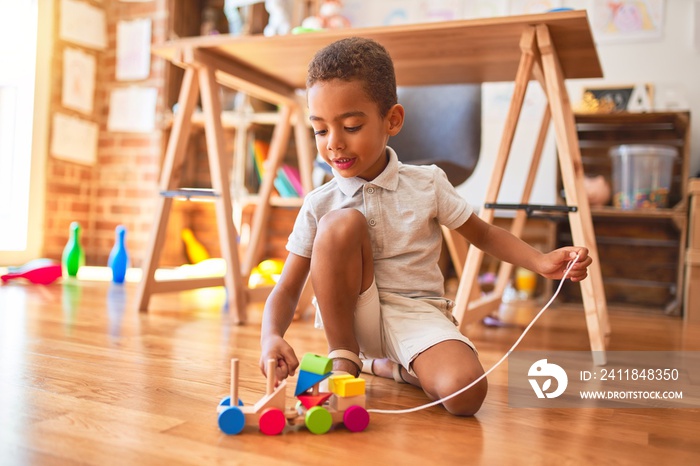 Beautiful african american toddler playing with wooden blocks train toy around lots of toys at kinde