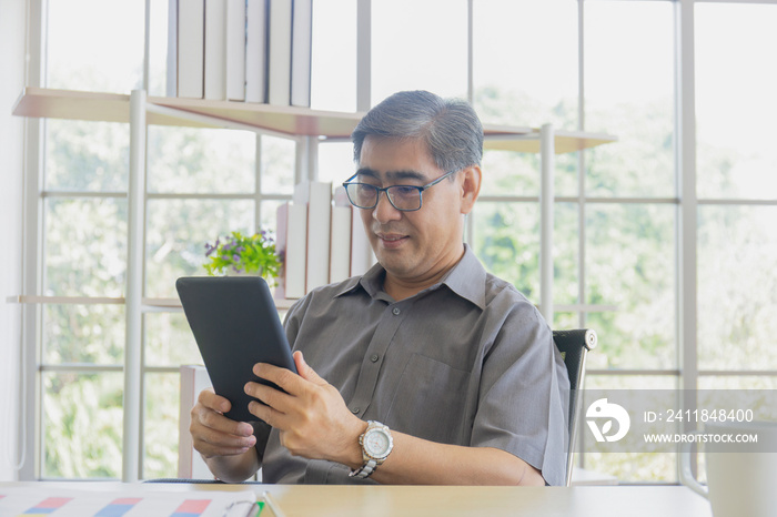 An Asian middle-aged man using an iPad in his hand.