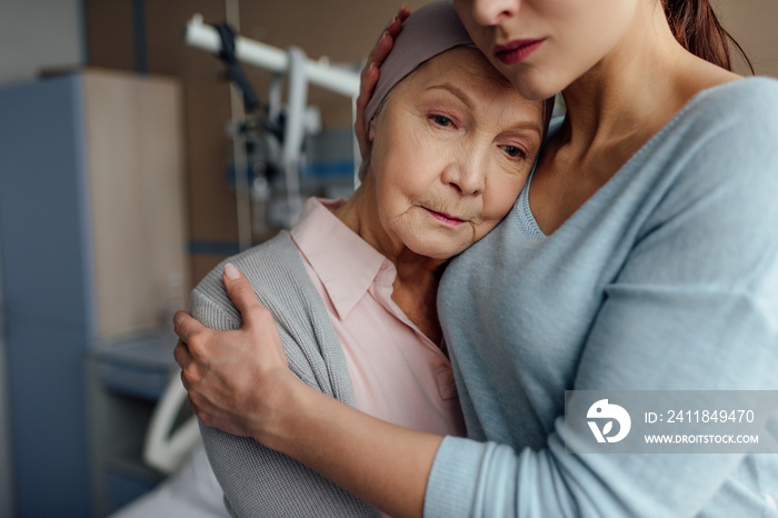 selective focus of daughter hugging sick senior mother with cancer in hospital