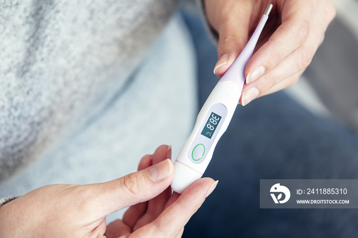 Womans hands hold thermometer that shows high body temperature