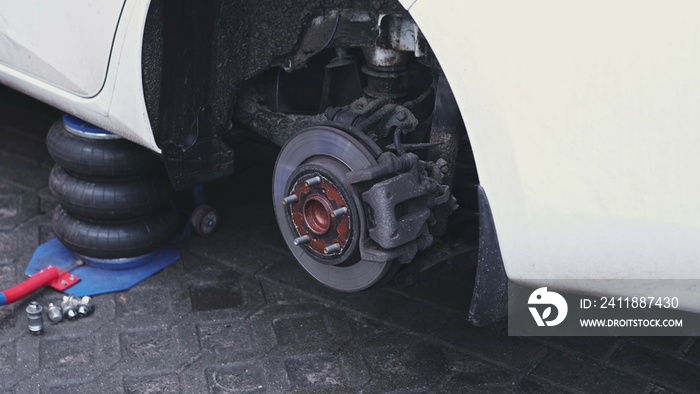 Car Wheel Hub with Brake Disc and Brake Pad Exposed during Tyre Change at Garage Workshop with Lug N