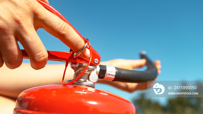 MACRO: Young woman pulls safety pin out of a fire extinguisher before using it