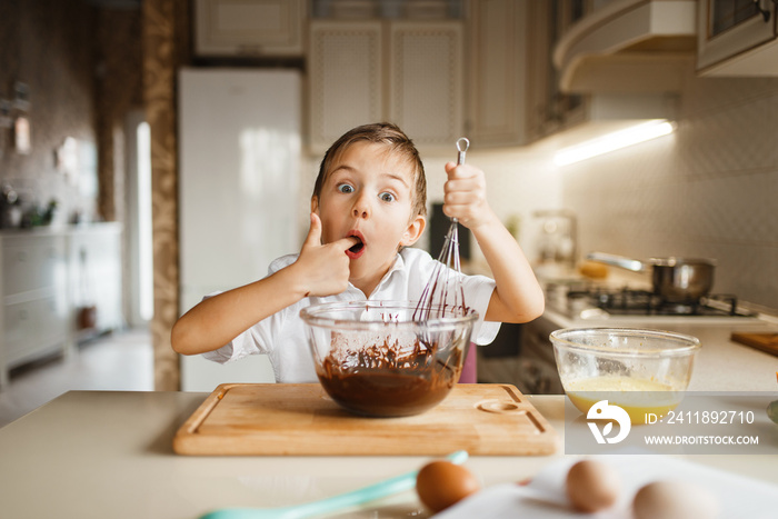 Male kid tastes melted chocolate in a bowl