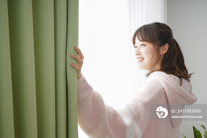 Young woman opening a curtain when getting up 