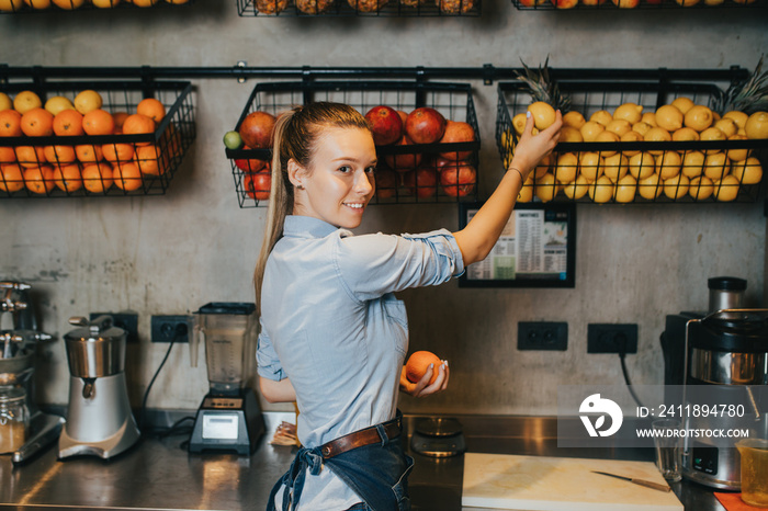 Happy young female bartender standing at juice bar counter and working.