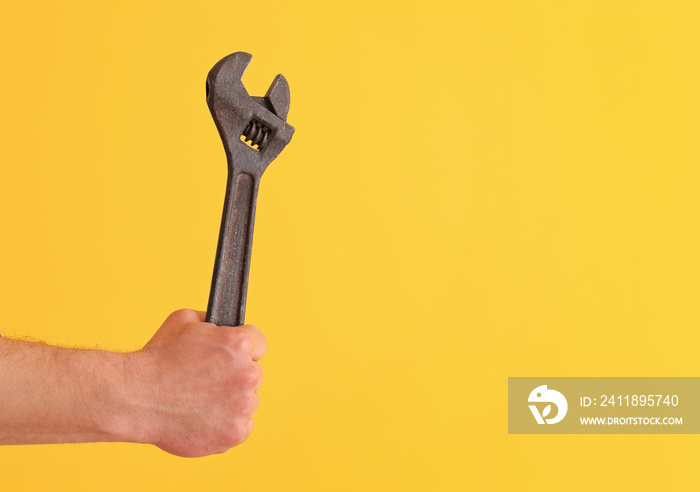 Hand of plumber with wrench on color background