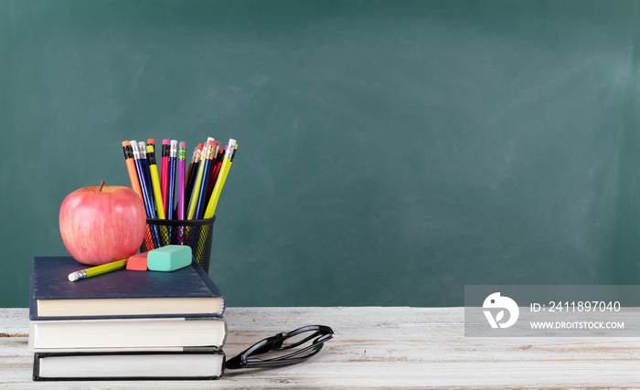 Back to school concept including books and stationery supplies with green chalkboard in background