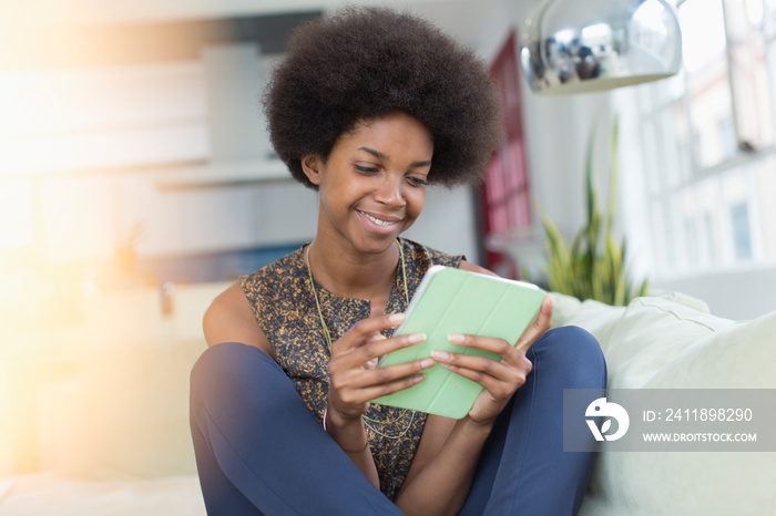 Smiling young woman with afro using digital tablet on sofa