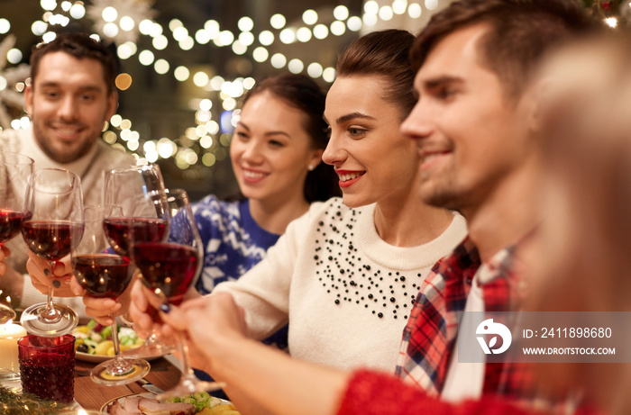 holidays and celebration concept - happy friends having christmas dinner at home, drinking red wine 