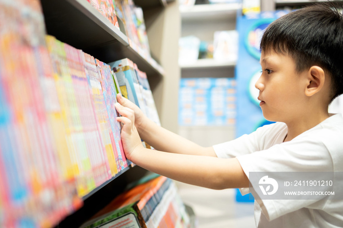 亚洲小孩在逛书店时选书，严肃的小男孩在寻找