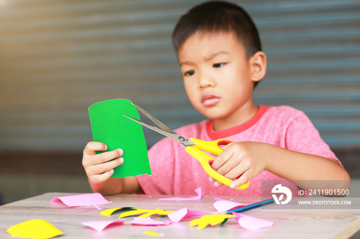 4-5岁亚洲男孩用剪刀在t上练习剪彩色纸的人像
